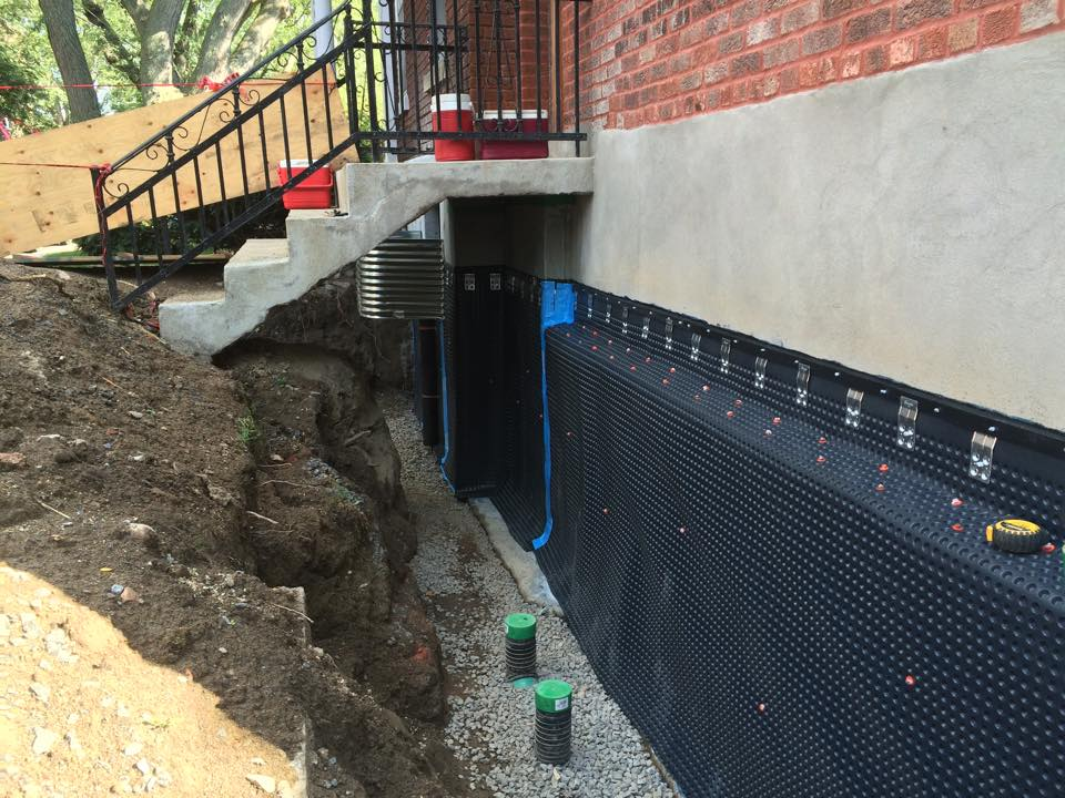 Side Yard Waterproofing & Parging project in Toronto — Narrow side yard excavated to the footing with dimple membrane fastened to a parged foundation wall and drainage cleanout risers in clear stone